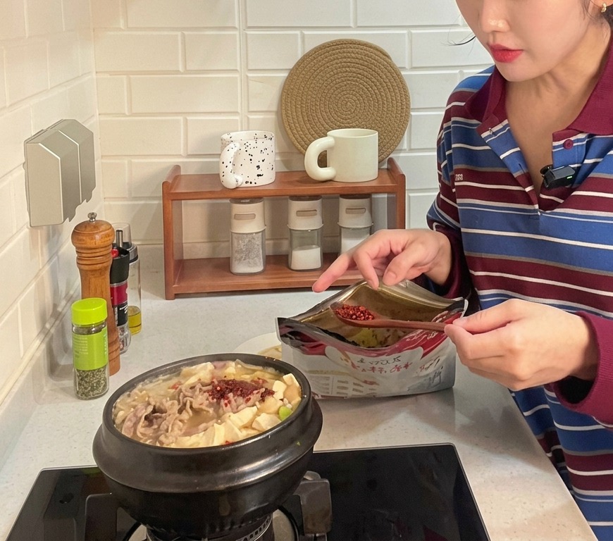 두부와 소고기가 듬뿍 들어간 뚝배기 된장찌개에 고춧가루 한 숟가락을 넣는 모습