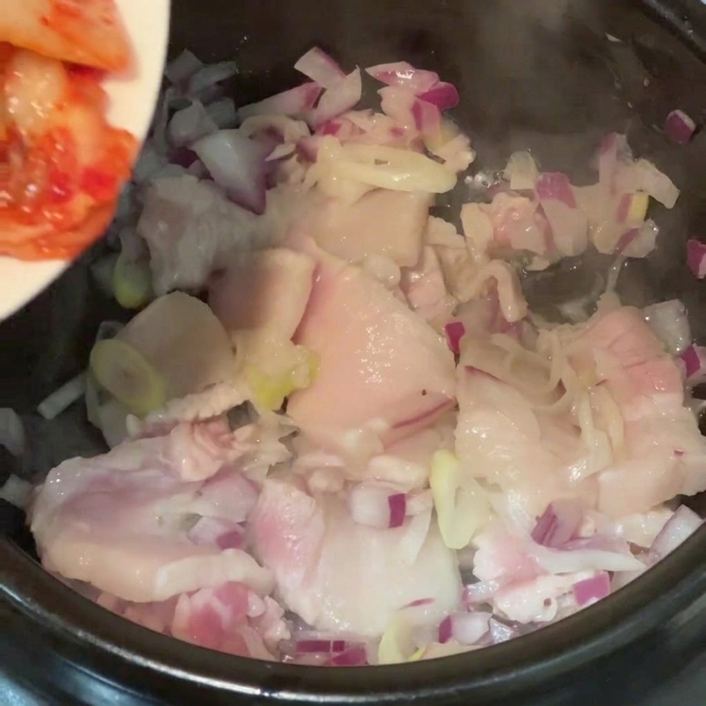 삼겹살을 볶던 냄비에 먹기 좋게 자른 신김치를 넣는 모습.