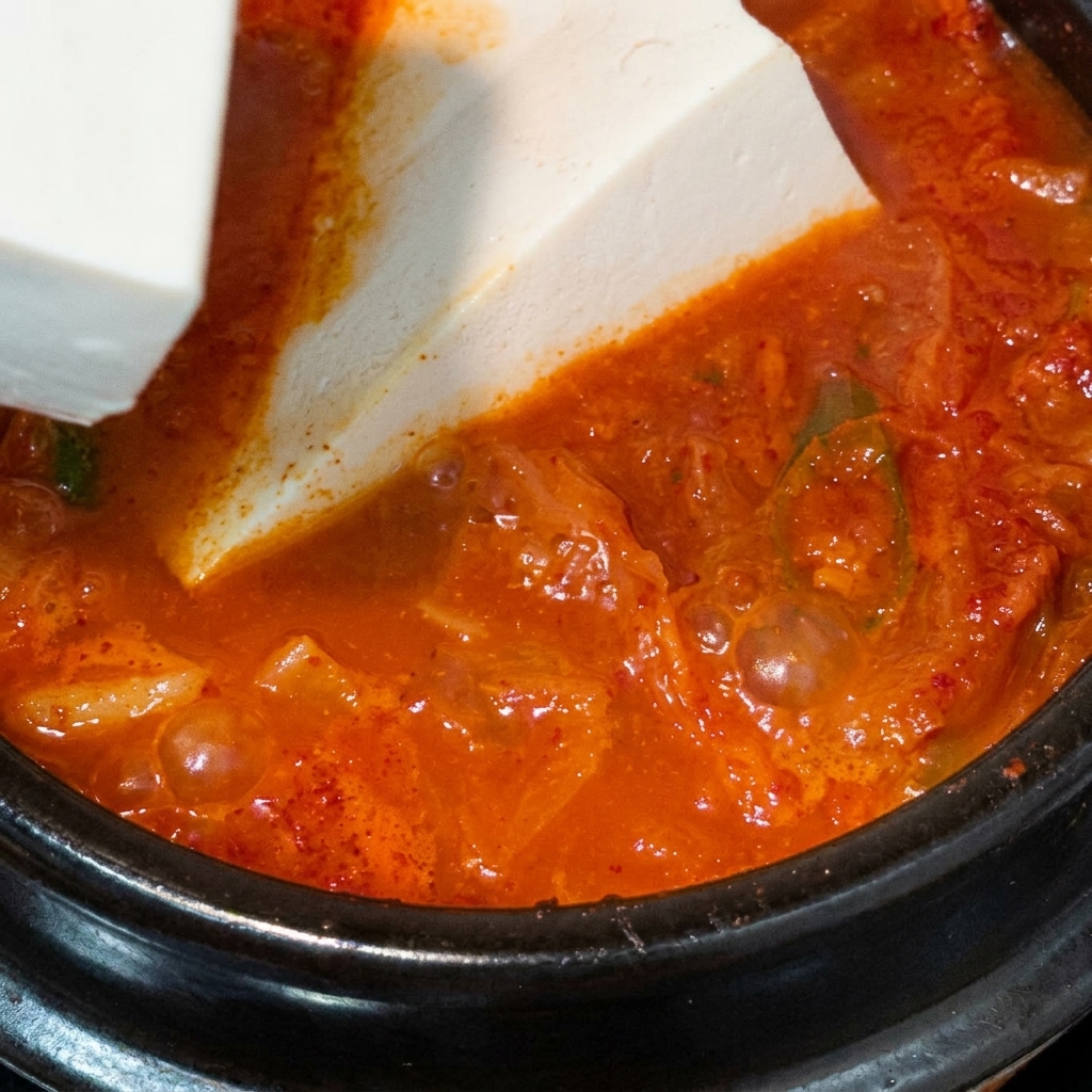 끓고 있는 붉은 김치찌개에 큼지막한 연두부를 조심스럽게 넣는 모습.