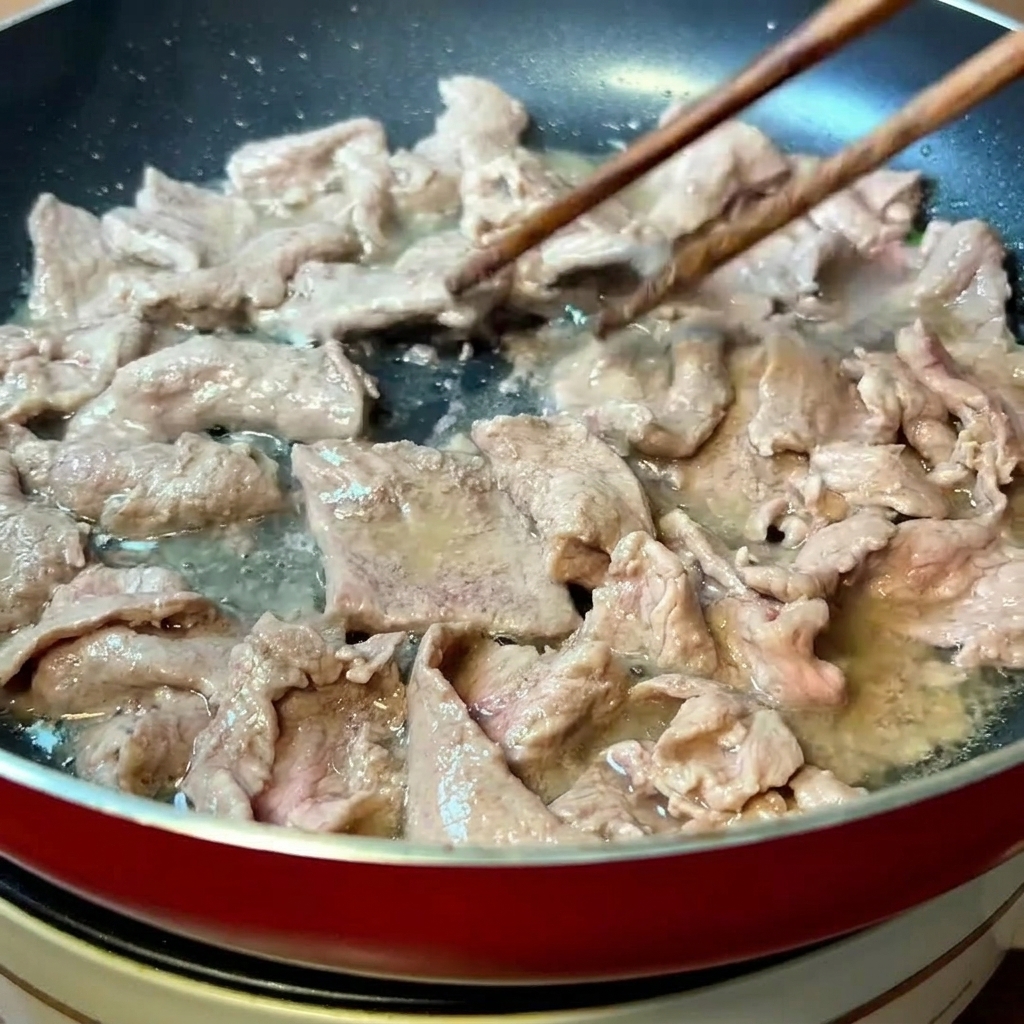 달궈진 팬에서 나무 젓가락으로 소고기를 빠르게 볶는 모습.