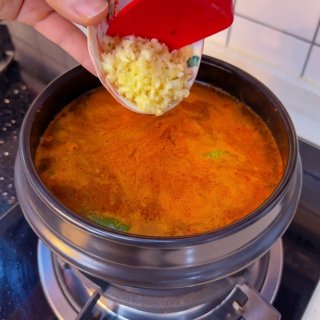 작은 그릇에 담긴 다진 마늘을 끓는 찌개에 넣는 모습.