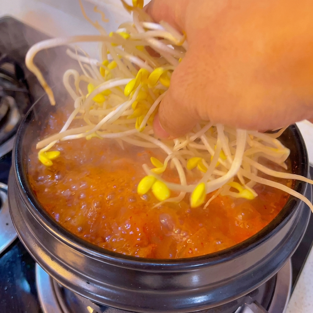 끓는 찌개에 신선한 콩나물을 한 줌 넣는 모습.