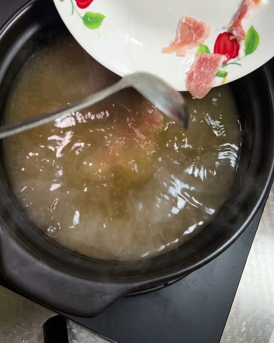 주황색 당근과 연노란색 감자 조각을 끓는 찌개에 넣는 모습.