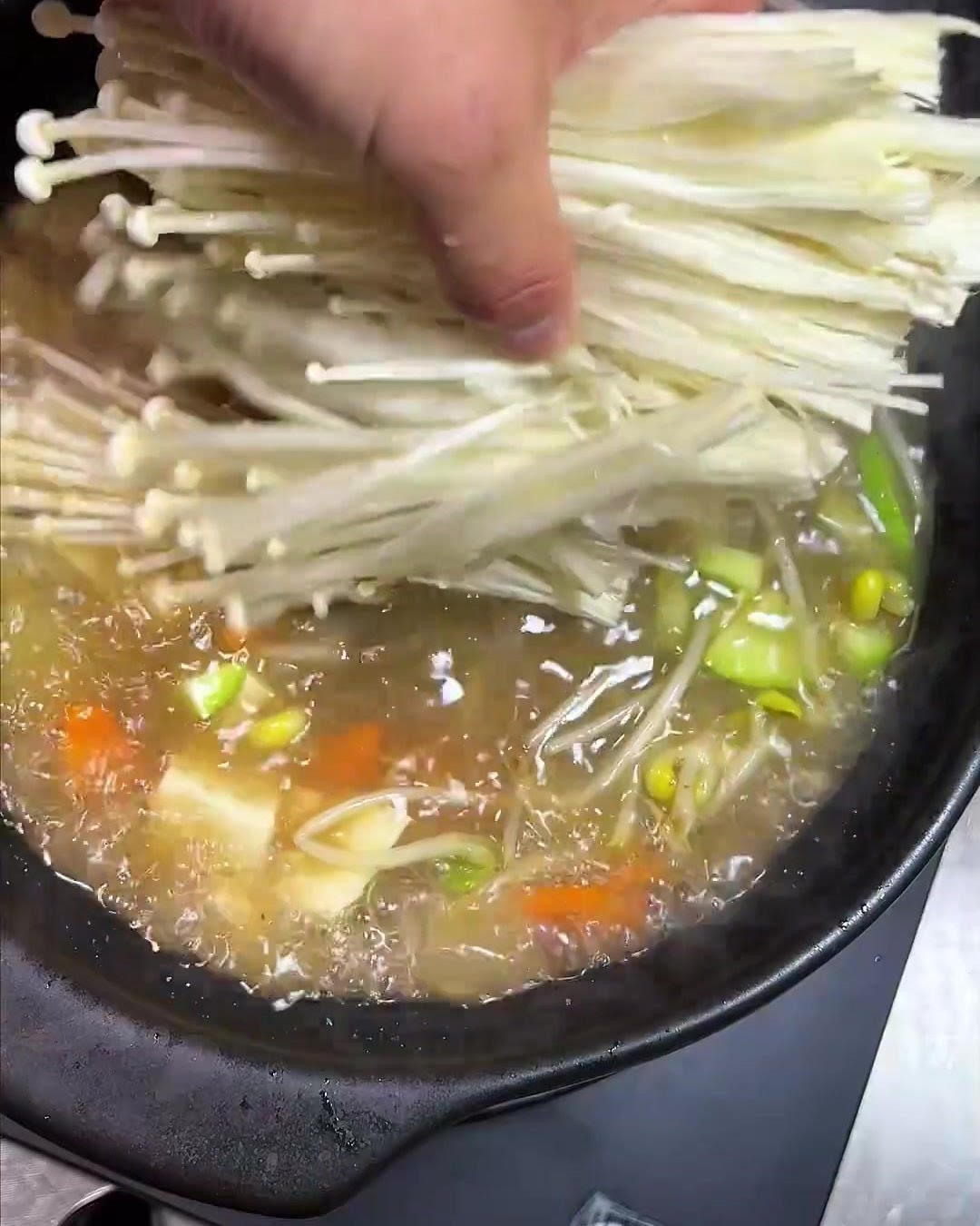 가늘고 긴 팽이버섯 한 줌을 끓고 있는 냄비에 넣는 모습.