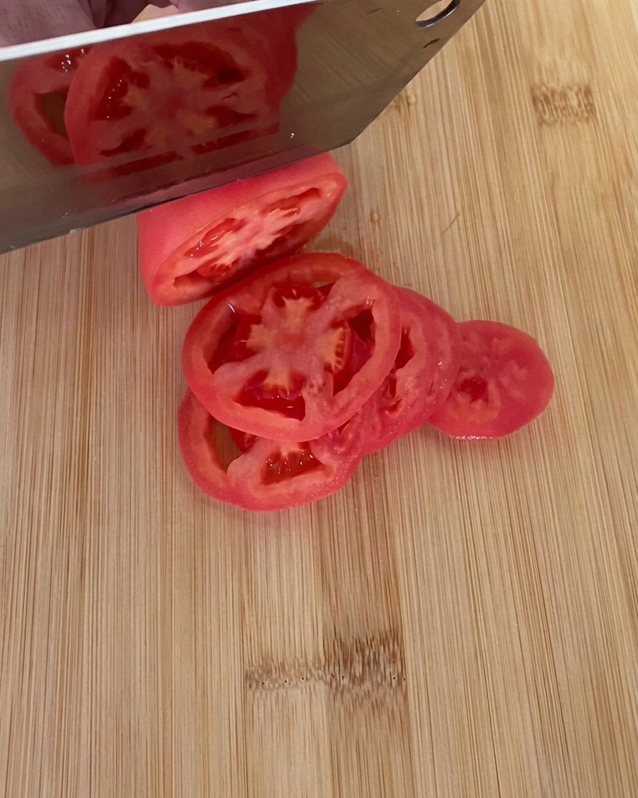 도마 위에서 잘 익은 붉은 토마토를 칼로 둥글고 두툼하게 써는 모습.