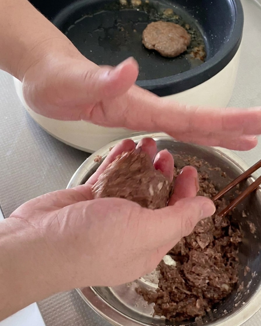 양손으로 생 소고기 반죽을 둥근 버거 패티 모양으로 던지며 빚는 모습.