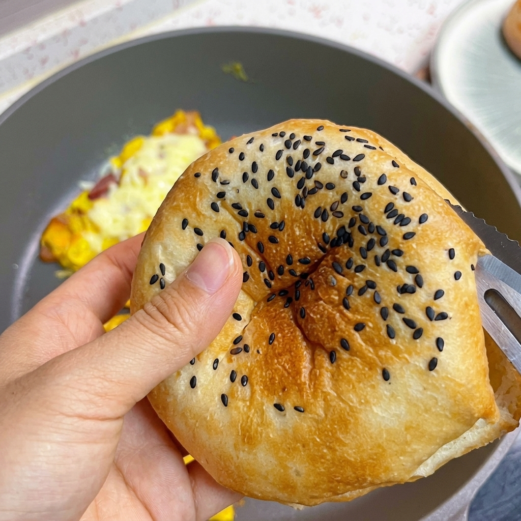 검은깨가 뿌려진 노릇한 버거 번을 반으로 자르는 모습.