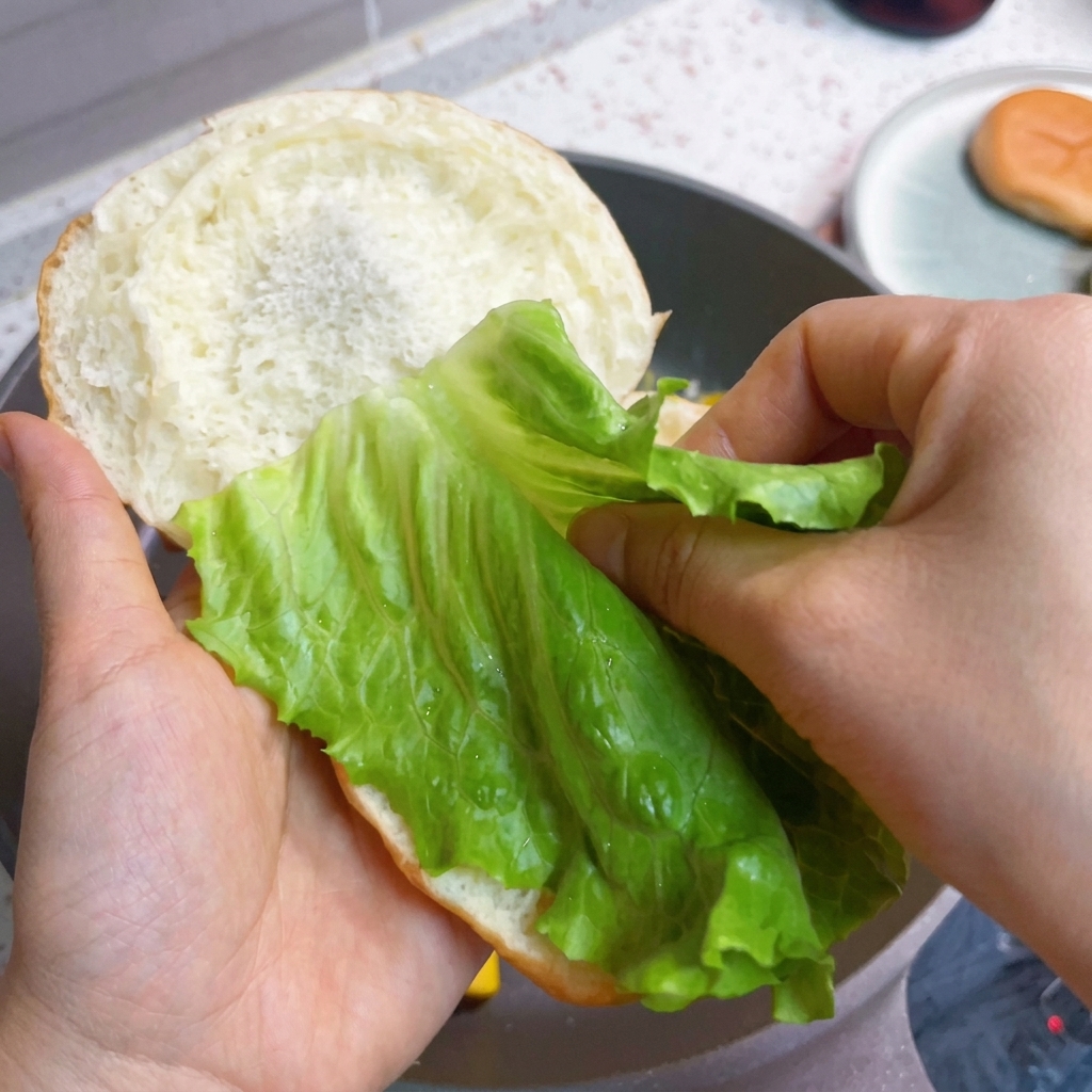 번 위에 신선한 상추, 베이컨, 푹신한 계란을 순서대로 쌓아 올리는 모습.