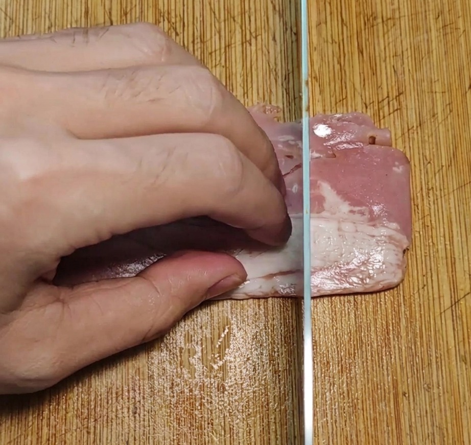 도마 위에서 베이컨을 한입 크기의 직사각형으로 일정하게 써는 모습.