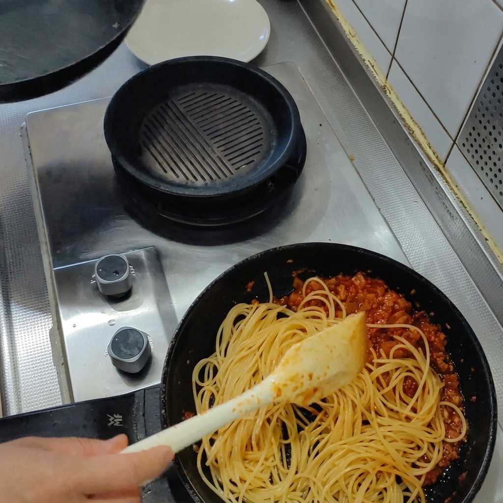 삶은 스파게티 면을 토마토 소스 팬에 넣는 모습.