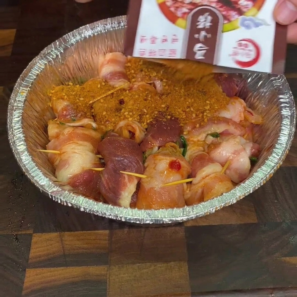알루미늄 용기에 담긴 삼겹살 말이 위로 바비큐 시즈닝 가루를 뿌리는 모습.