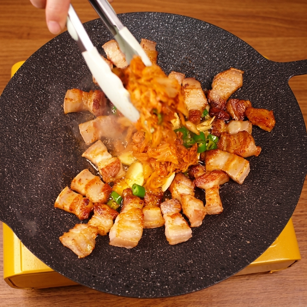 집게로 삼겹살과 김치를 함께 볶아내는 모습.