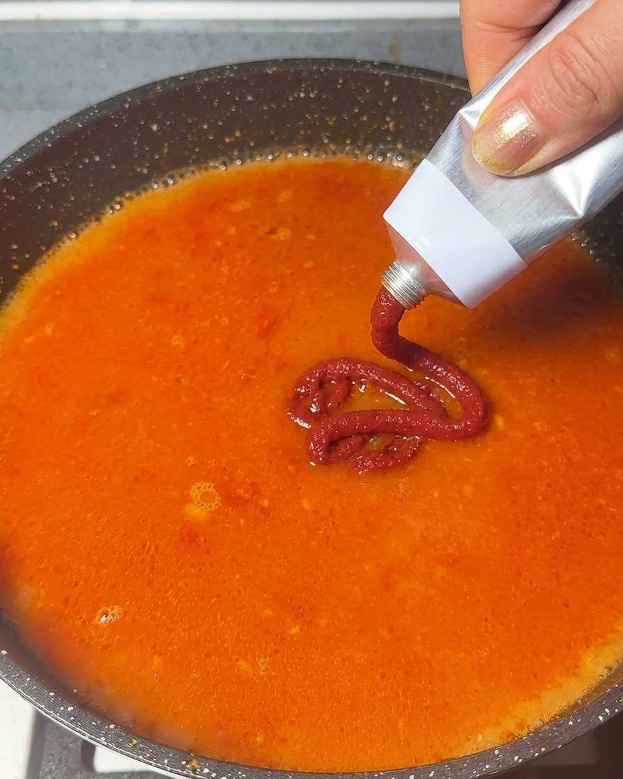 주황빛으로 끓어오르는 육수에 튜브형 토마토 페이스트를 짜 넣는 모습