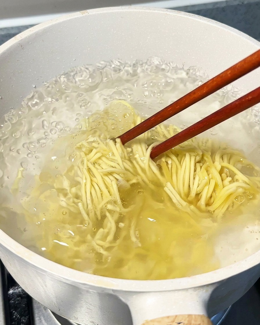 끓는 물이 담긴 큰 냄비에 라멘 면을 넣고 젓가락으로 젓는 모습