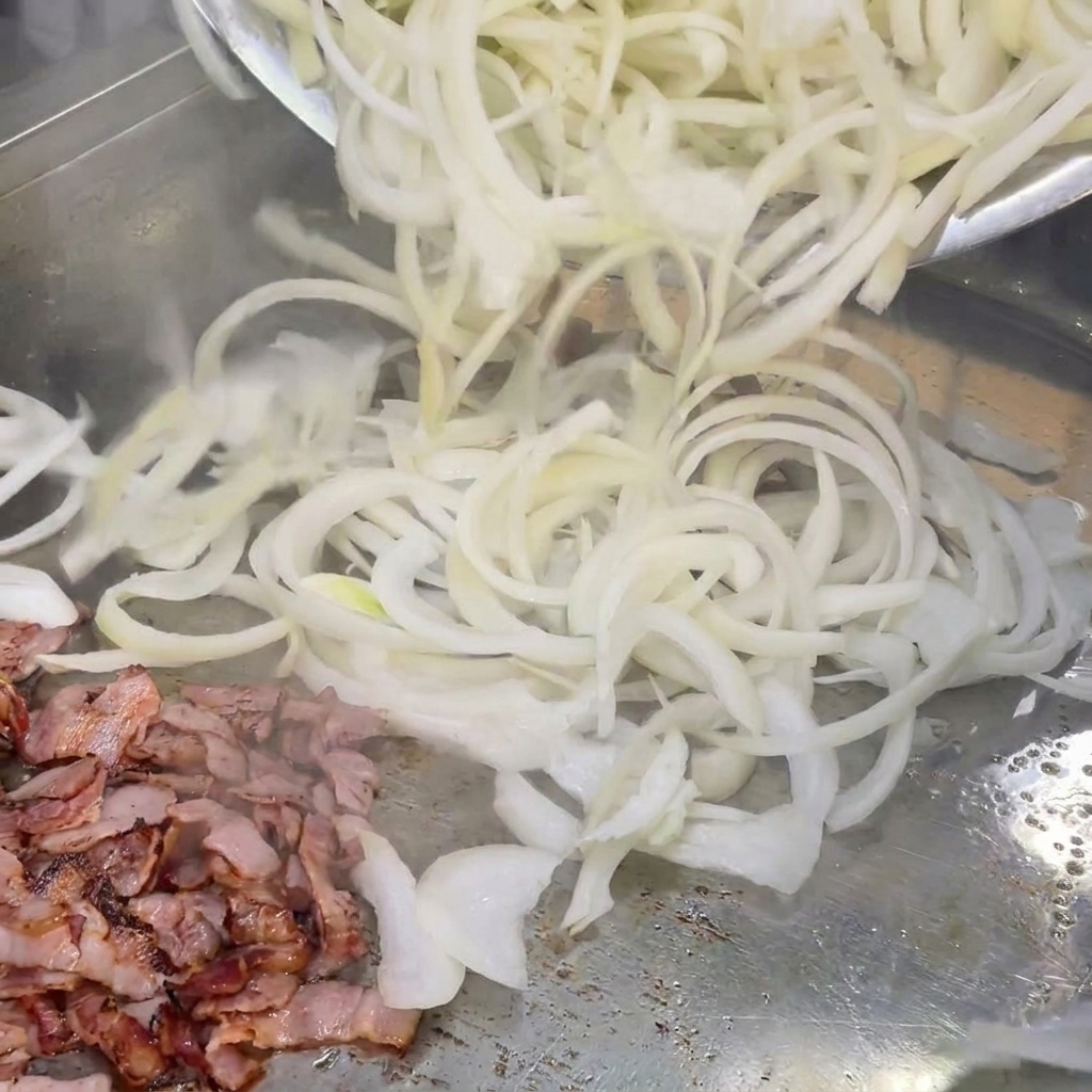 그릴 위에서 베이컨 조각과 섞이는 채 썬 흰 양파.