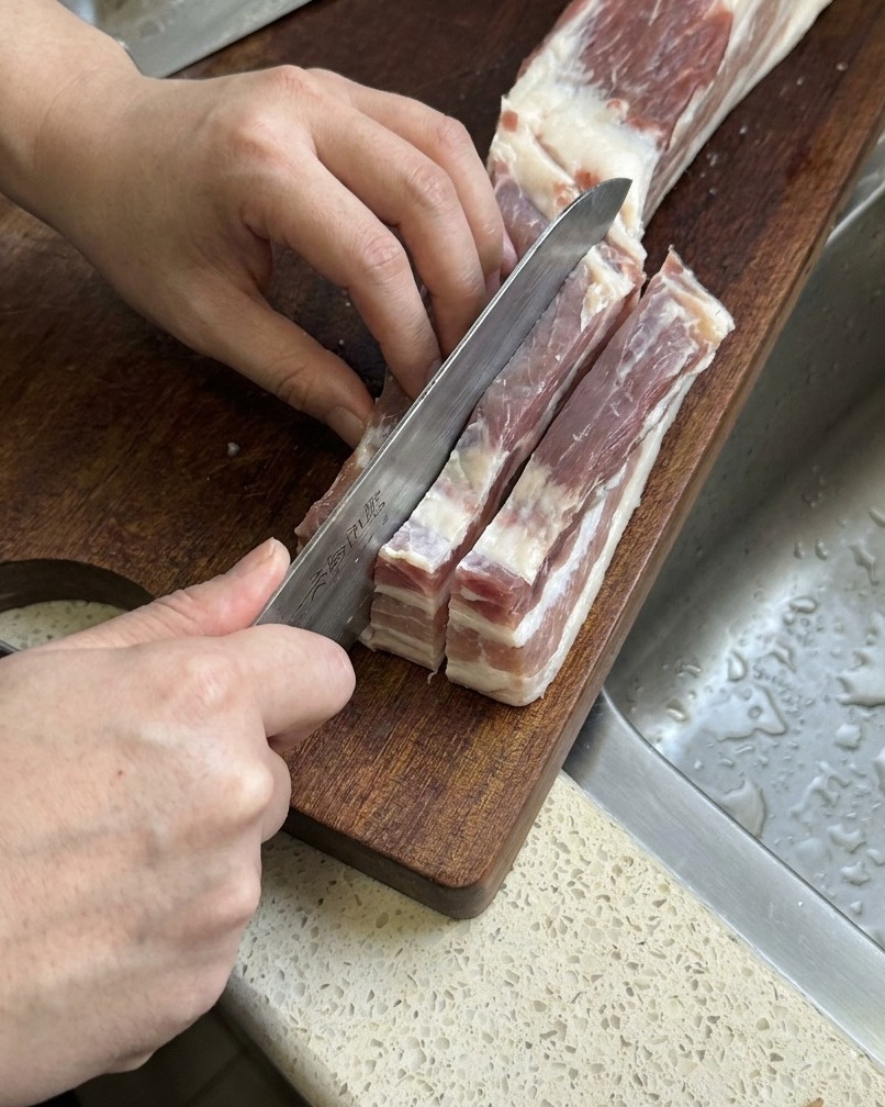 날카로운 칼로 길고 두꺼운 줄 모양으로 썰고 있는 삼겹살.
