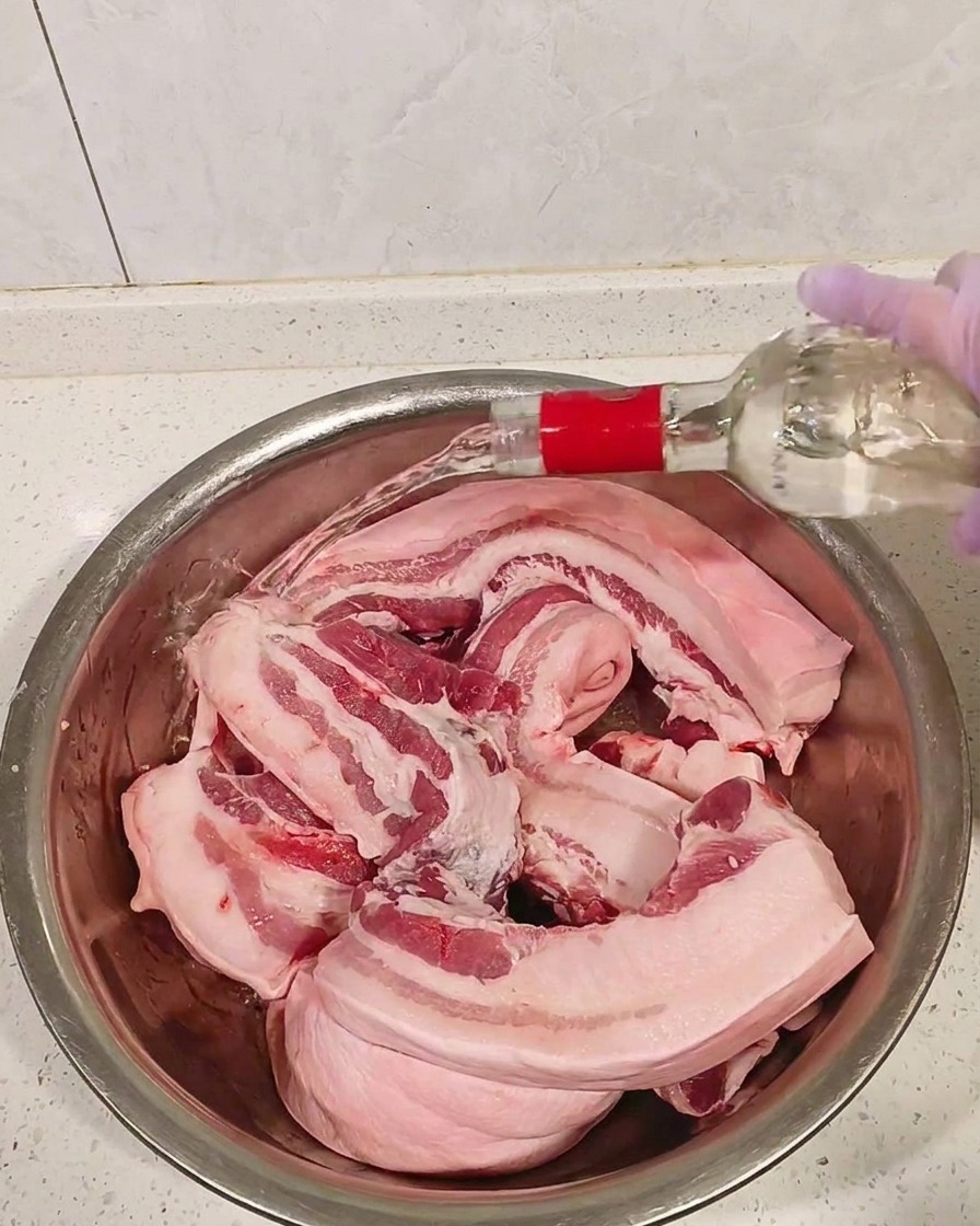금속 볼에 담긴 생삼겹살에 투명한 고도주를 붓는 모습.