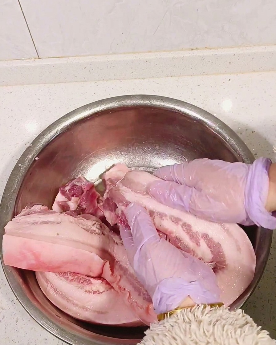 보라색 장갑을 낀 손으로 삼겹살에 술을 마사지하듯 바르는 모습.