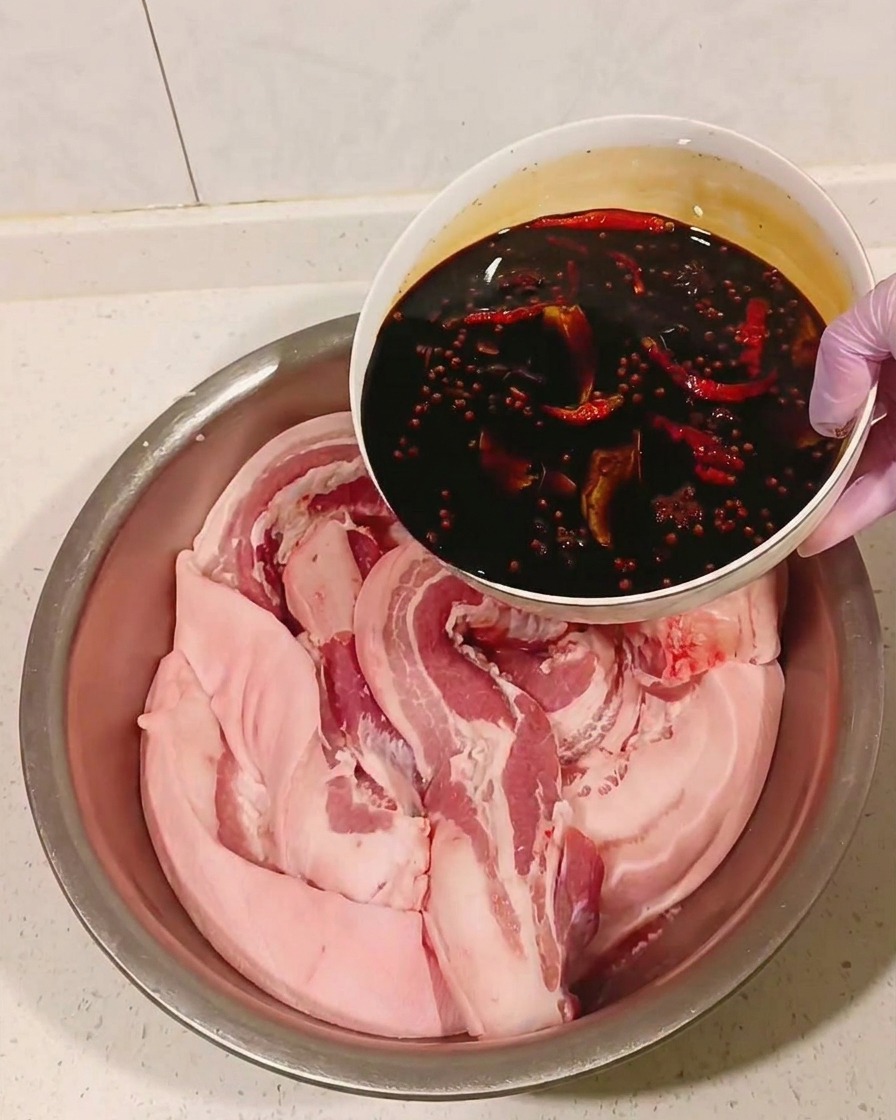 식힌 향신료 간장 소스를 볼에 담긴 삼겹살 위로 붓는 모습.