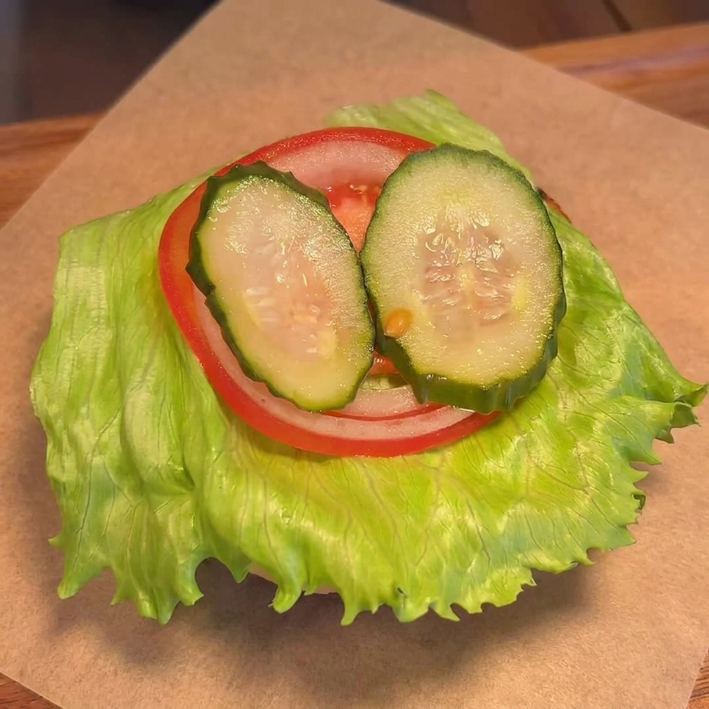 채소를 얹은 번 위에 잘 녹은 치즈가 덮인 소고기 패티를 올리는 모습.