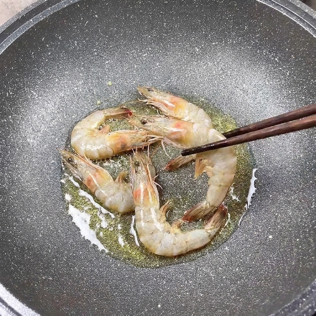 뜨거운 팬에서 노릇하게 익어가는 새우를 젓가락으로 뒤집는 모습.