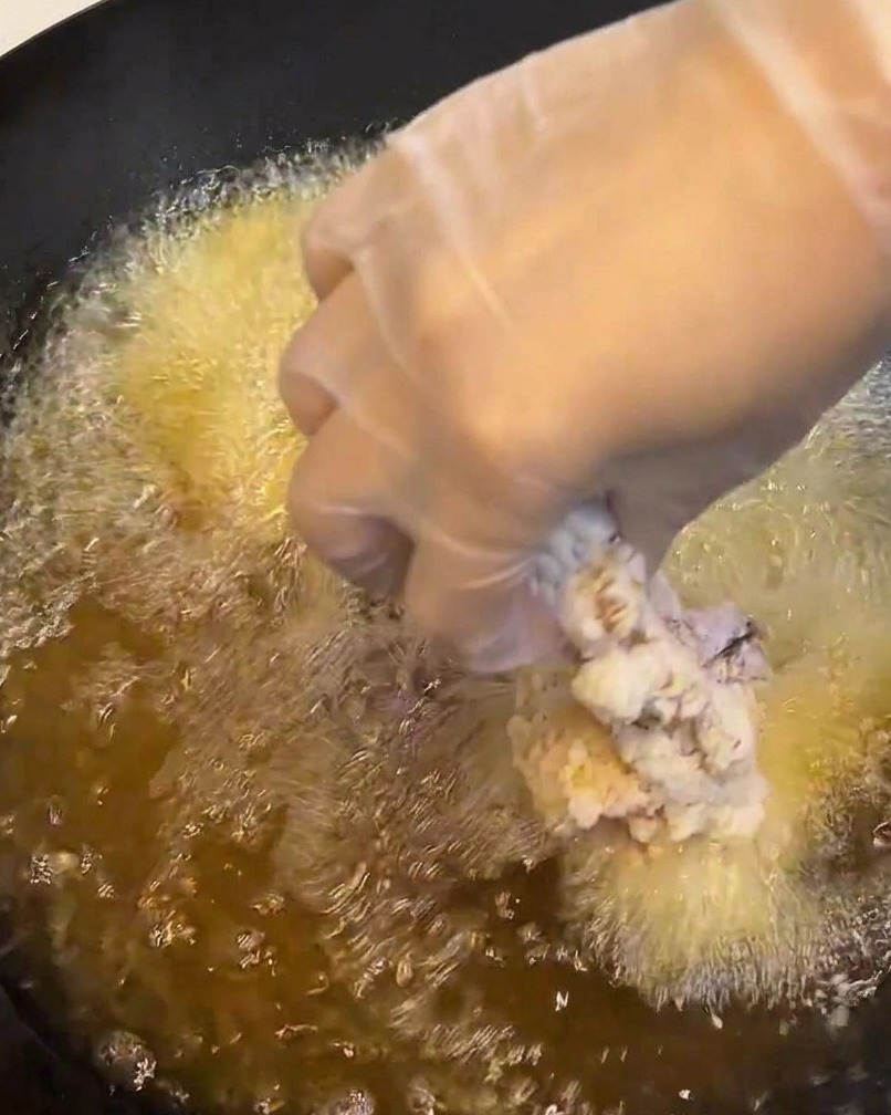 끓는 기름에 빵가루 입힌 닭고기를 조심스럽게 넣는 모습.
