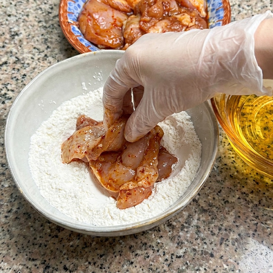 마리네이드한 닭다리살을 마른 밀가루 반죽이 담긴 볼에 누르는 모습.
