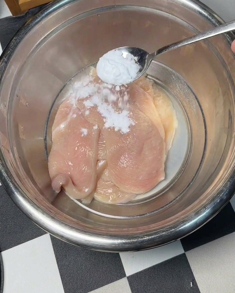 금속 볼에 담긴 닭고기 위로 베이킹소다를 뿌리는 모습.