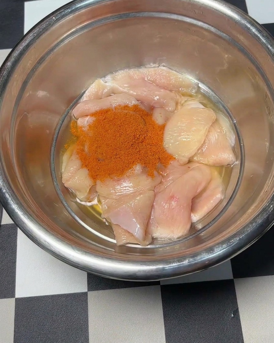 닭고기 조각 위로 붉은 뉴올리언스 마리네이드 가루를 붓는 모습.