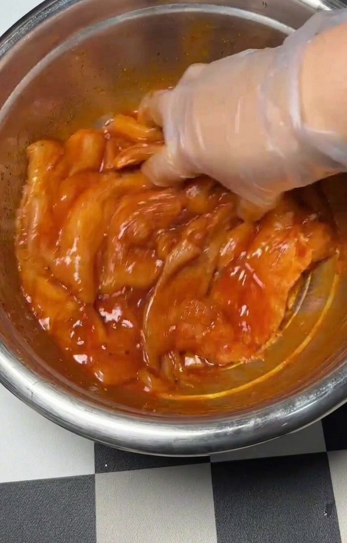 위생 장갑을 낀 손으로 볼 안의 닭고기와 양념을 골고루 섞는 모습.