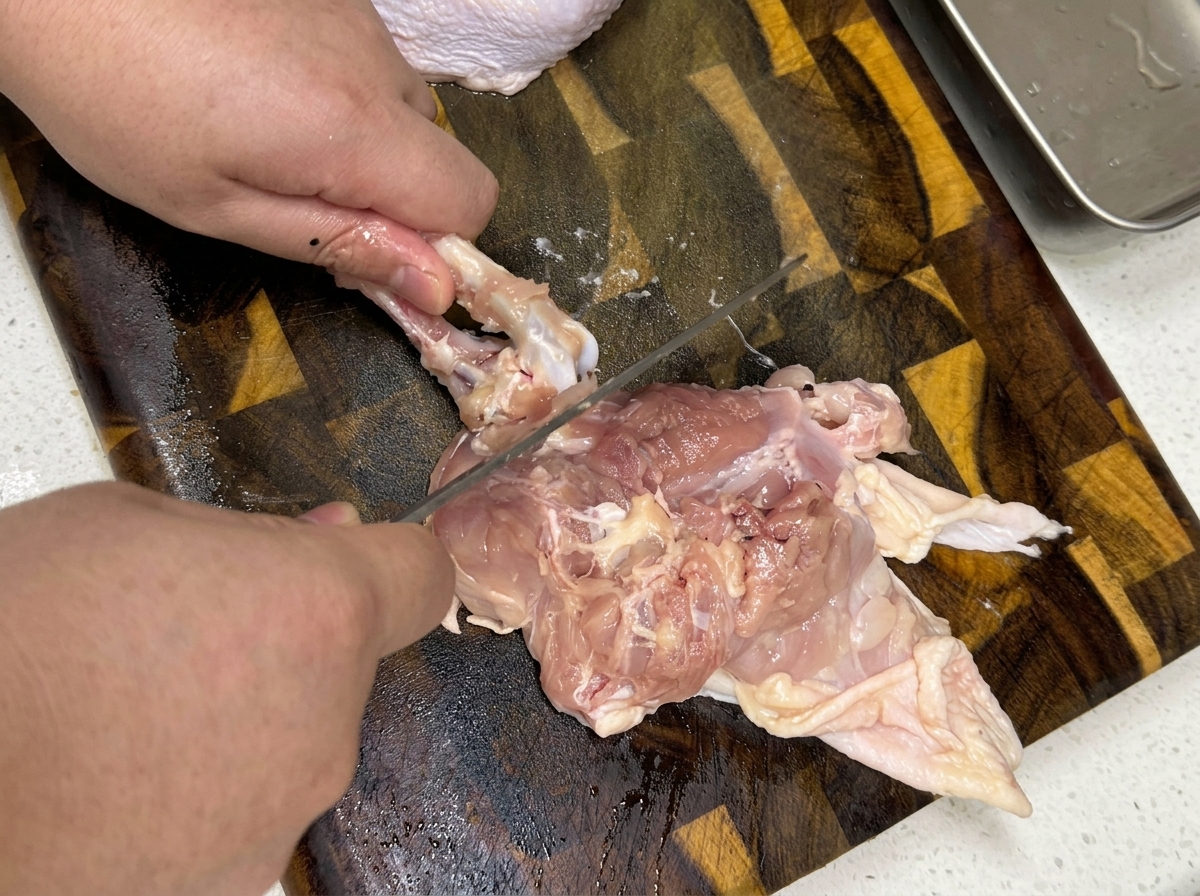 나무 도마 위에서 생닭다리살의 뼈를 제거하는 손의 모습.