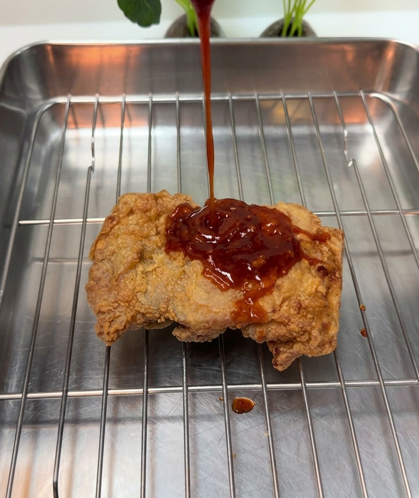 와이어 랙 위의 바삭한 치킨에 소스를 뿌리는 모습.