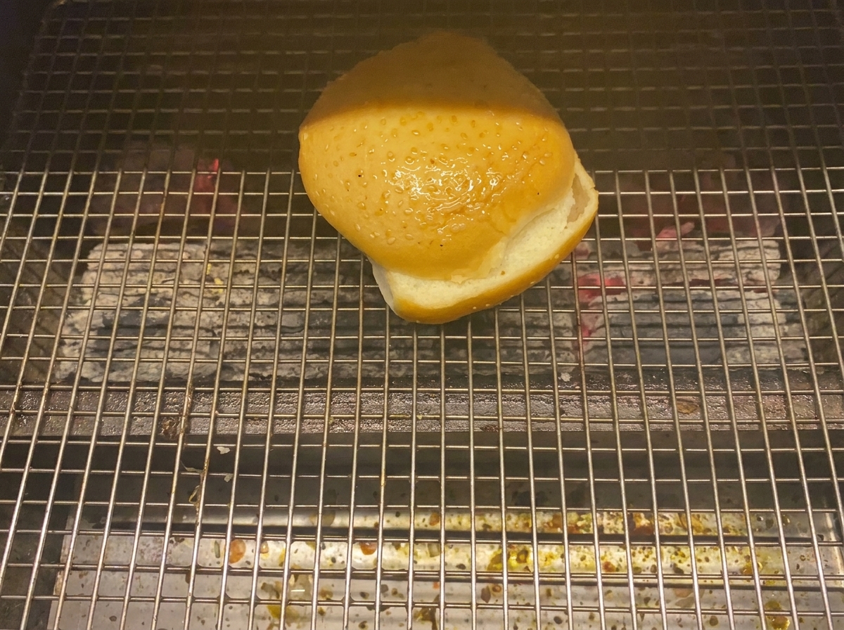숯불 그릴 위에서 뒤집어 구워지는 버거 번 반쪽.