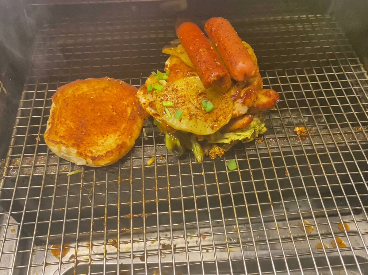 그릴망 위에서 구운 감자와 소시지, 각종 고기가 층층이 쌓인 거대한 버거와 구운 번.