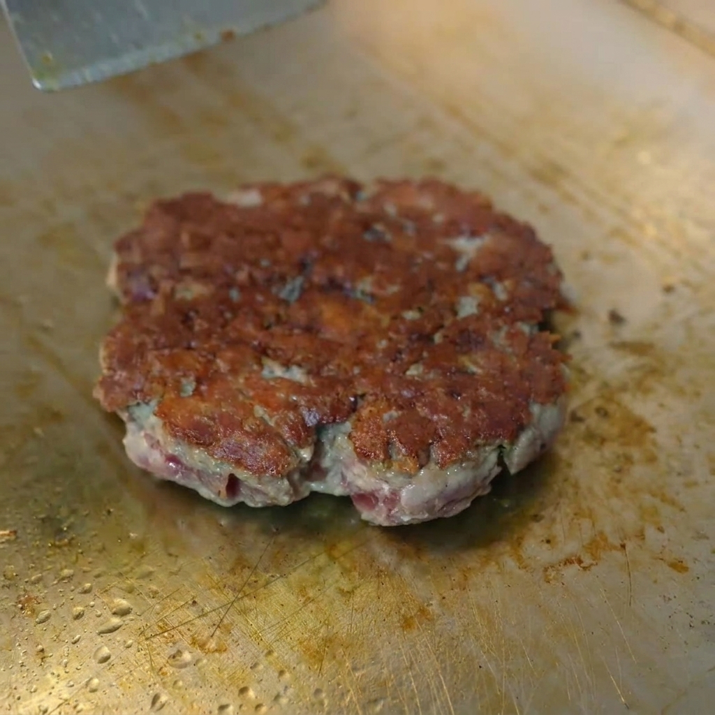 메탈 돔 아래에서 갈색으로 익은 소고기 패티 위로 녹아내리는 노란 치즈.