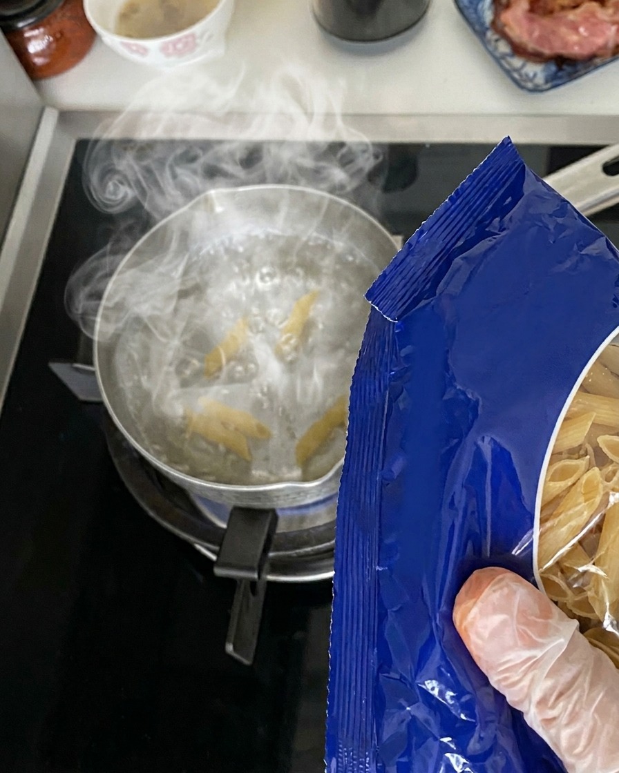 스토브 위에서 끓고 있는 냄비에 파란색 포장지에서 마른 펜네 파스타를 쏟아붓는 모습.