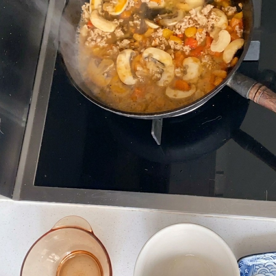 다진 돼지고기, 얇게 썬 버섯, 깍둑썰기한 토마토로 만든 소스가 검은색 프라이팬에서 보글보글 끓고 있는 모습.