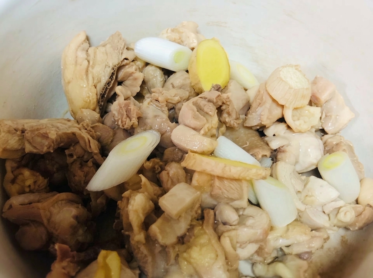 클레이 팟에 담긴 닭고기에 대파, 생강, 액체 양념을 넣는 모습.