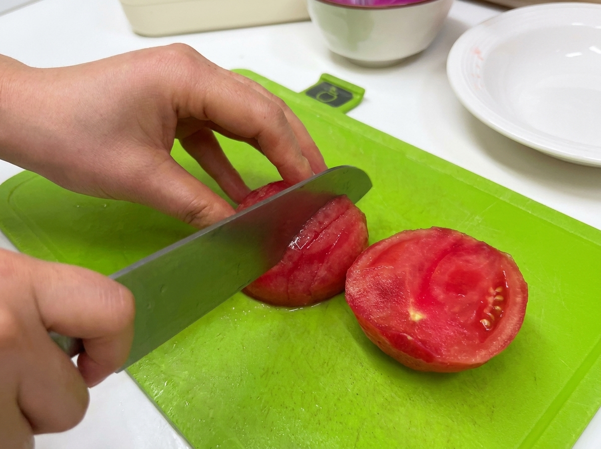 초록색 도마 위에서 큰 식칼을 사용해 껍질을 벗긴 붉은 토마토를 썰고 있는 모습.