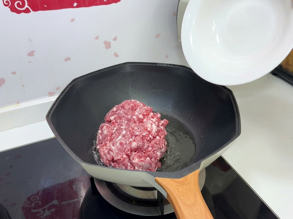 하얀 볼에 담긴 익히지 않은 돼지고기 다짐육을 기름을 두른 뜨거운 팬에 붓는 모습.