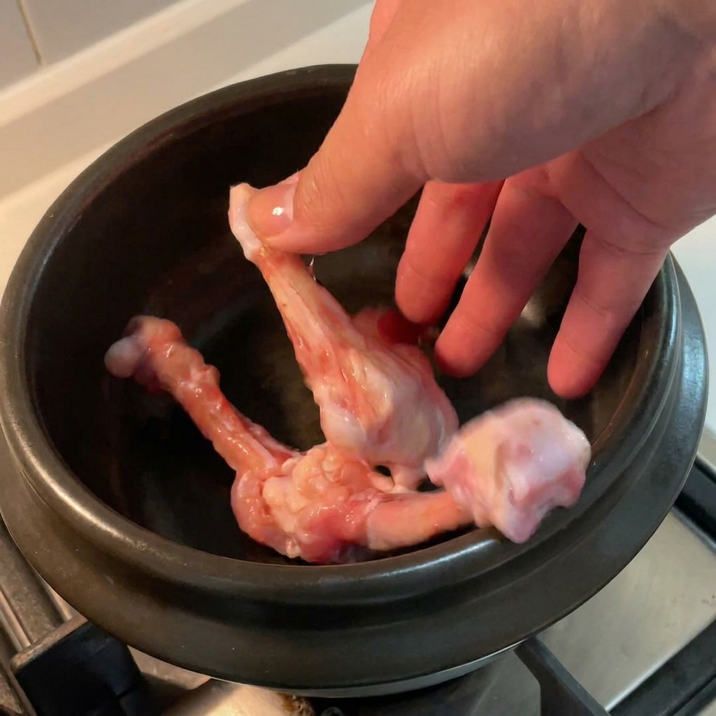 검은색 뚝배기 안에 날 닭다리뼈가 담겨 있는 모습.