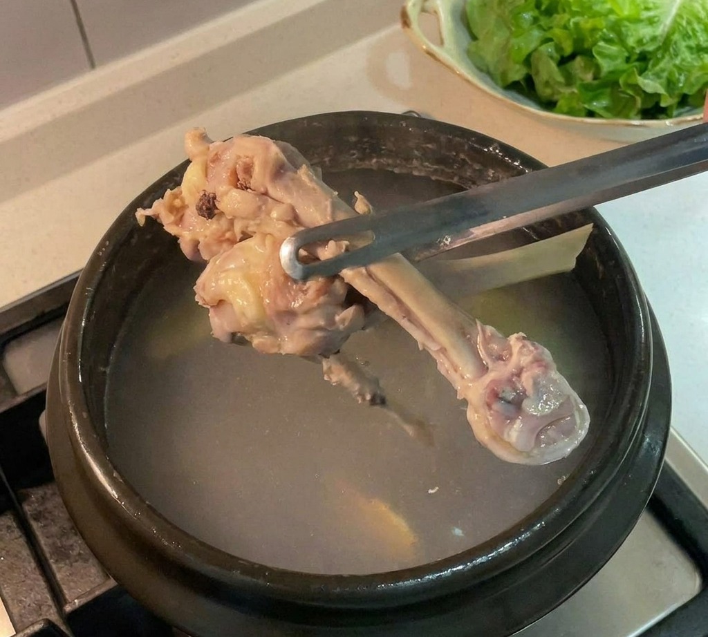 집게를 사용해 어두운 냄비에서 끓인 닭뼈를 건져내는 모습.