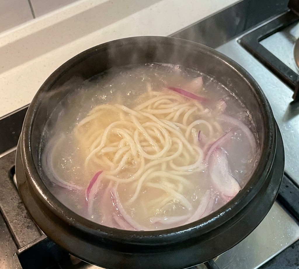 냄비 안에서 끓고 있는 육수와 면 위에 채 썬 적양파가 들어간 모습.
