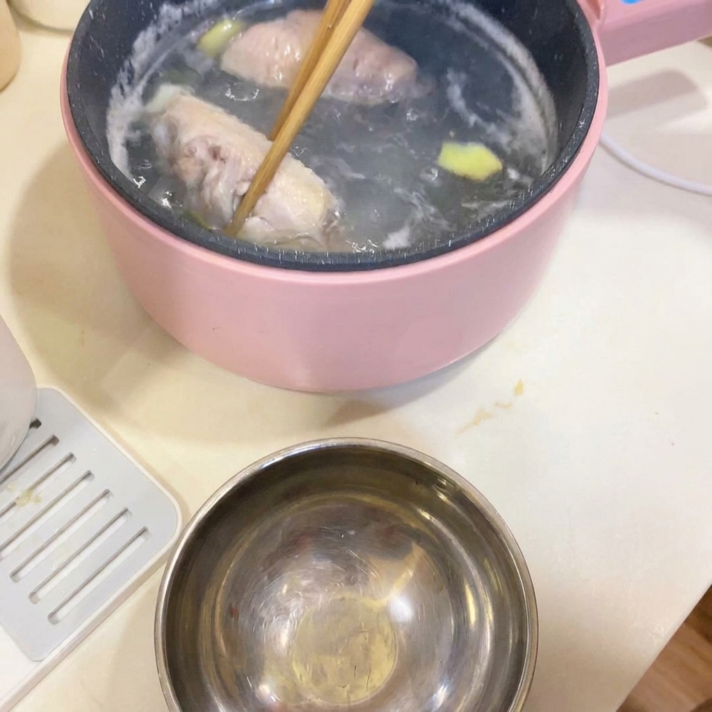 냄비에서 젓가락으로 데친 닭날개를 건져내는 모습.