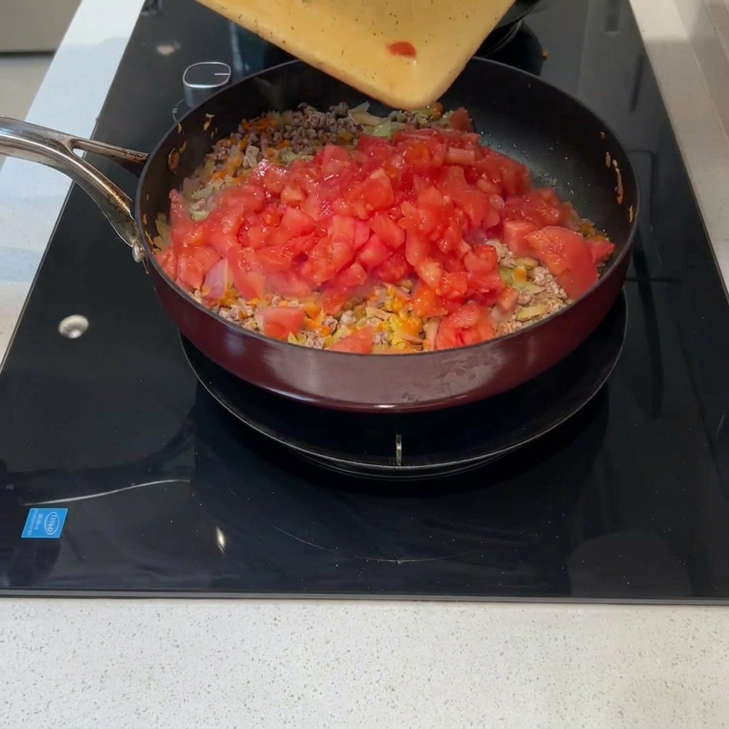 도마 위의 갓 다진 토마토를 고기와 채소가 있는 프라이팬으로 옮겨 담는 모습.