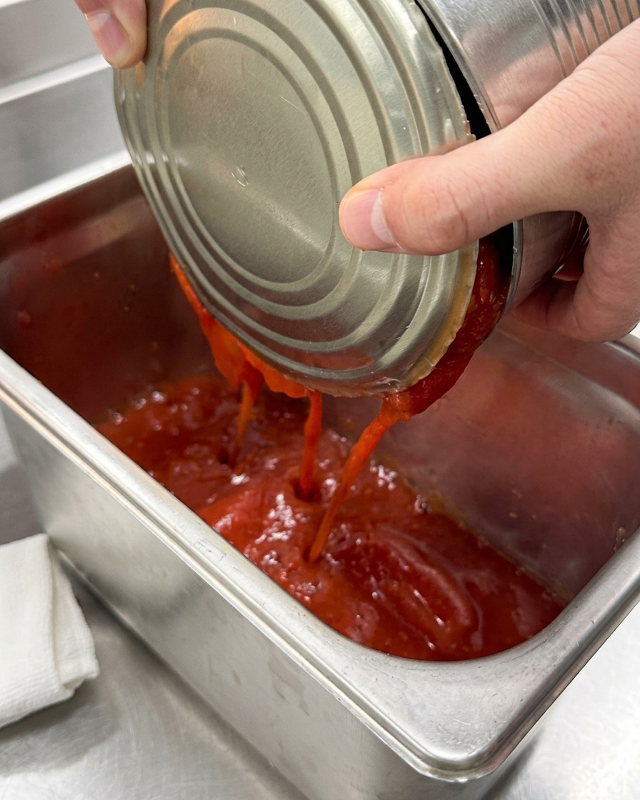 깨끗한 스테인리스 팬에 껍질을 벗긴 통조림 토마토를 붓는 모습.