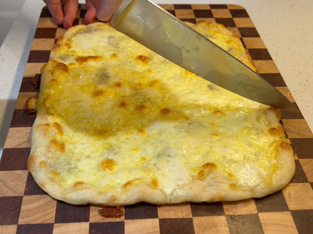 치즈가 끓어오르는 갓 구운 피자를 도마 위에서 큰 식칼로 자르는 모습.