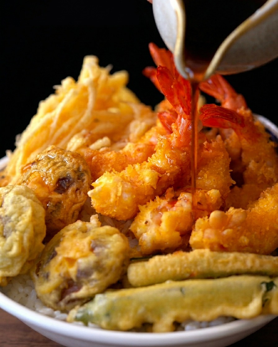 따뜻한 밥 위에 튀김을 올리고 간장 소스를 붓는 모습
