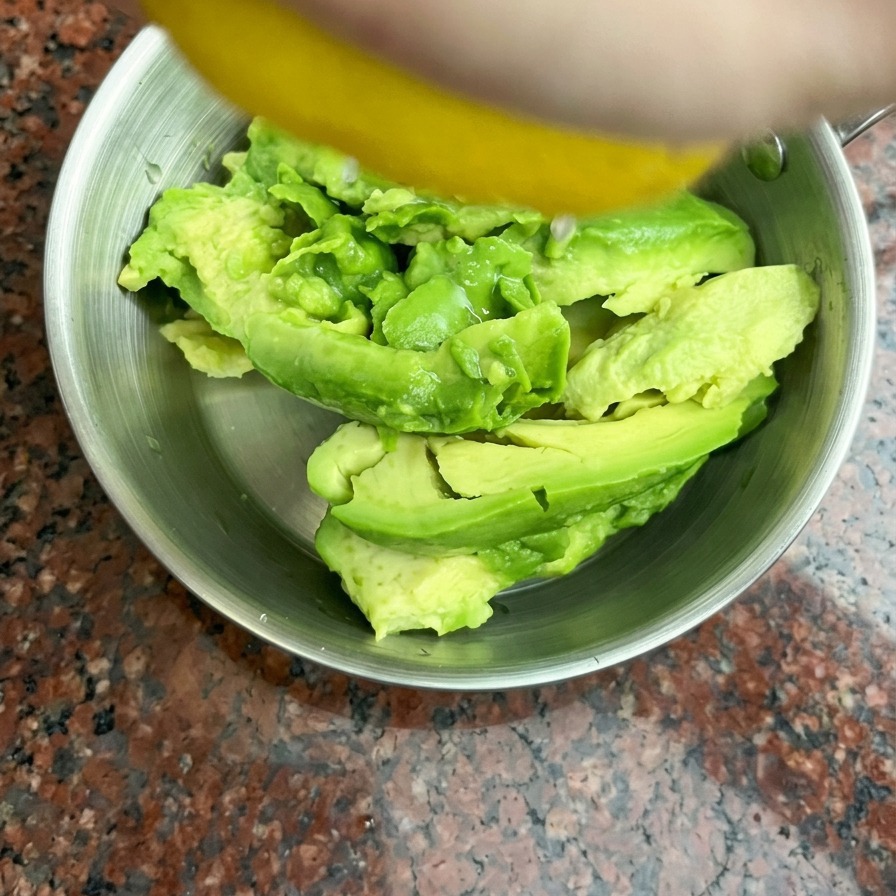 스테인리스 볼 안에 반으로 잘라 둔 아보카도 위로 손으로 신선한 레몬즙을 짜 넣는 모습.