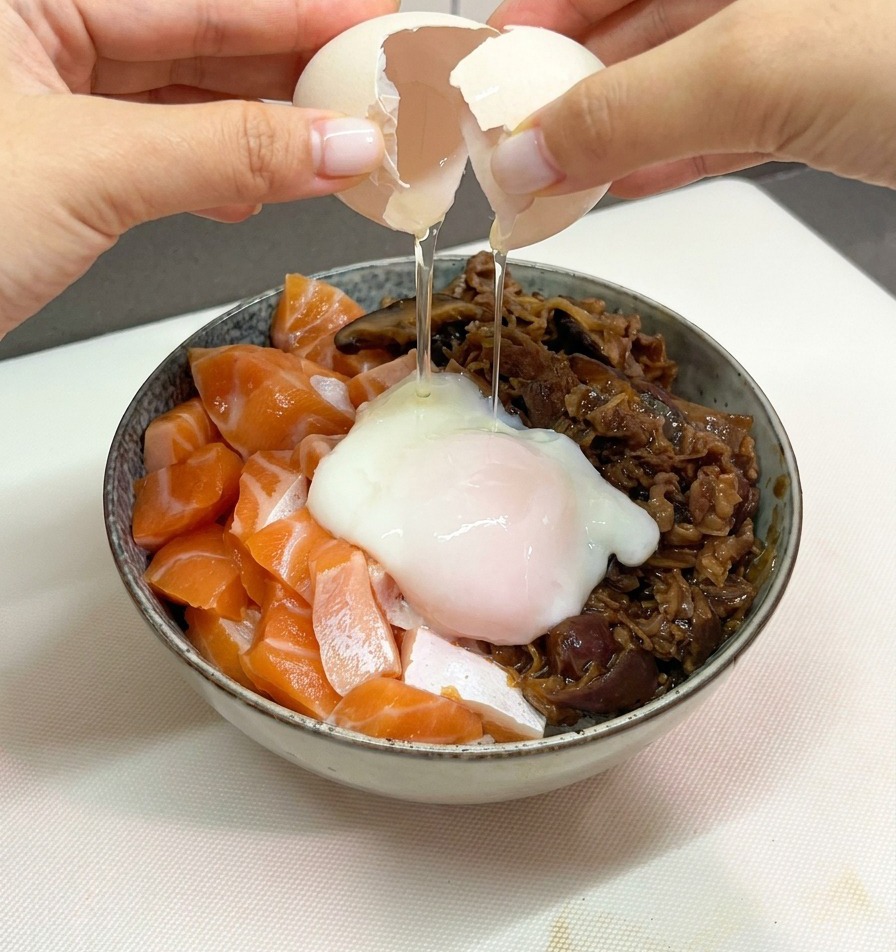 연어와 소고기 덮밥 가운데에 부드러운 온센타마고를 조심스럽게 깨뜨려 올리는 손.